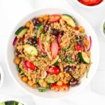 A bowl of mixed chickpeas, quinoa, onion, olives, tomatoes, and fresh basil.