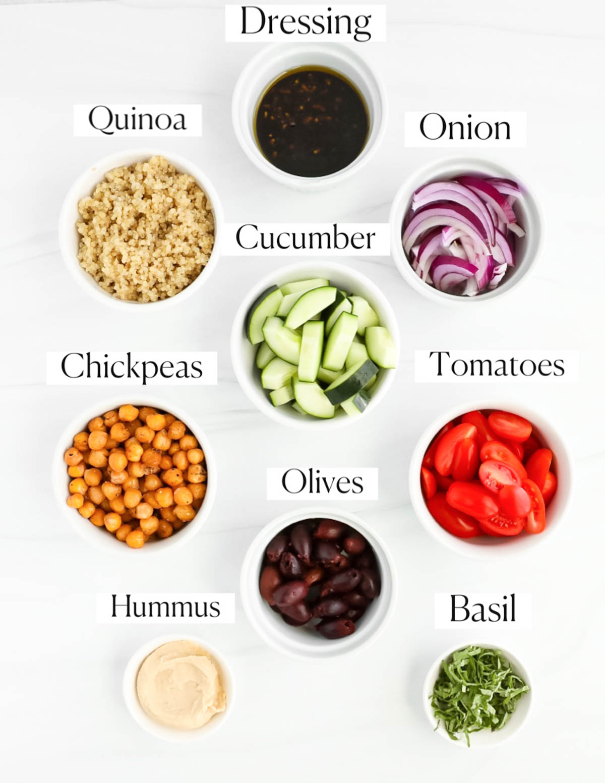 Labeled ingredients in small white bowls including: dressing, quinoa, onion, cucumber, chickpeas, tomatoes, olives, basil, and hummus.