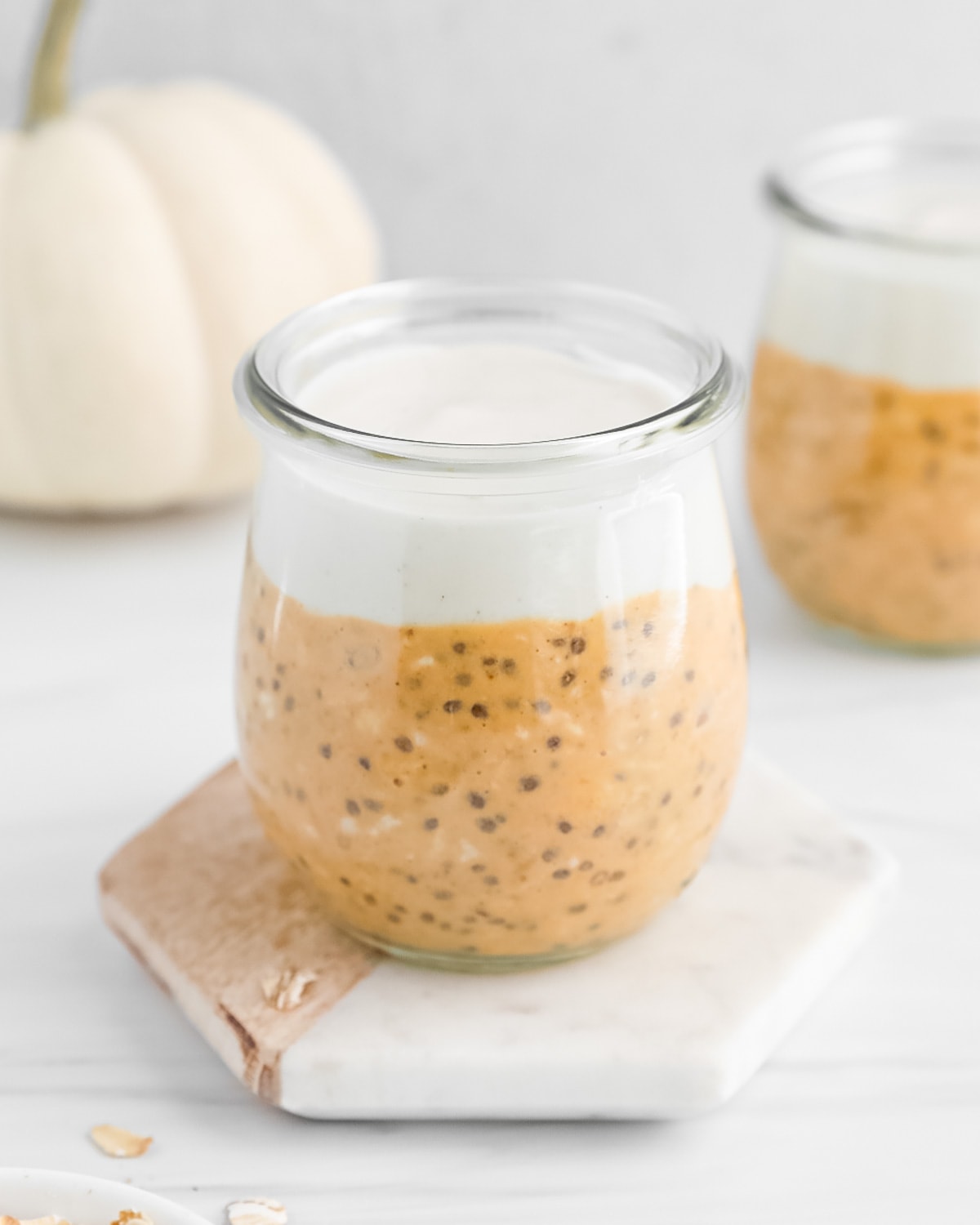 A clear glass filled with pumpkin overnight oats and vanilla yogurt.