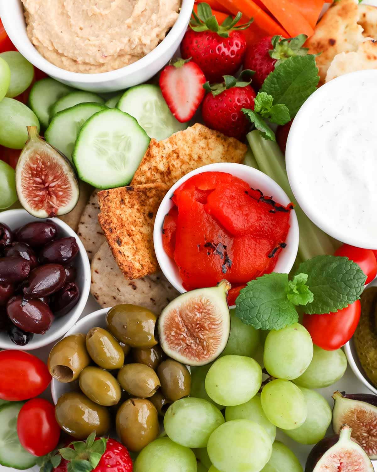Hummus, tzatziki, peppers, olives, cucumbers, strawberries, figs, mint leaves, tomatoes.