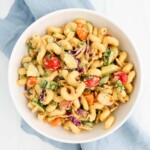 A white bowl filled with pasta salad with vegetables, cilantro, and a creamy dressing.