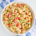 A round bowl filled with shell pasta, red peppers, celery, and pickles.