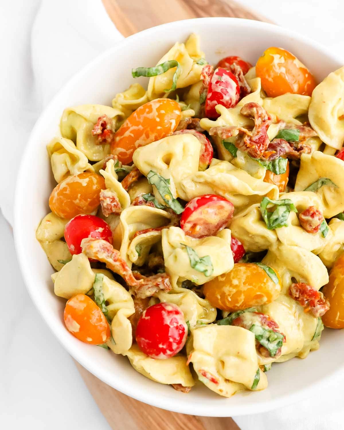 A close-up picture of tortellini covered in a creamy avocado pesto dressing tossed with tomatoes and fresh basil.